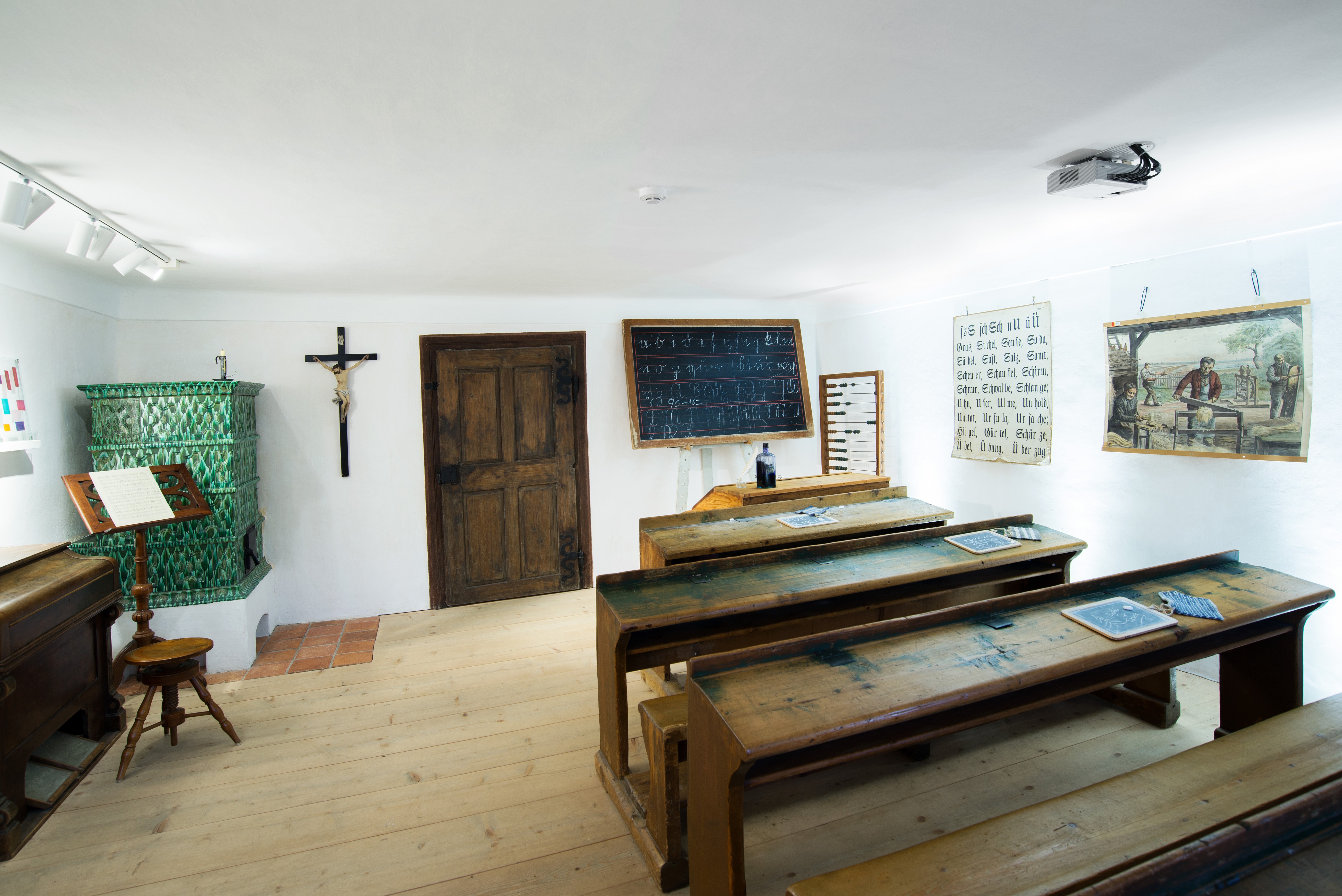 La vecchia aula scolastica nel museo di Arnsdorf, con i banchi di legno, la cattedra il grande crocifisso alla parete e la stufa di maiolica verde