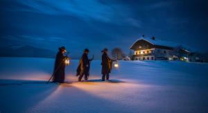 Tre scampanatori "Anglöckler" camminano verso una casa nella neve alla luce di lanterne