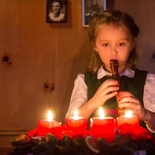 Una bambina suona il flauto davanti a 4 candele rosse accese