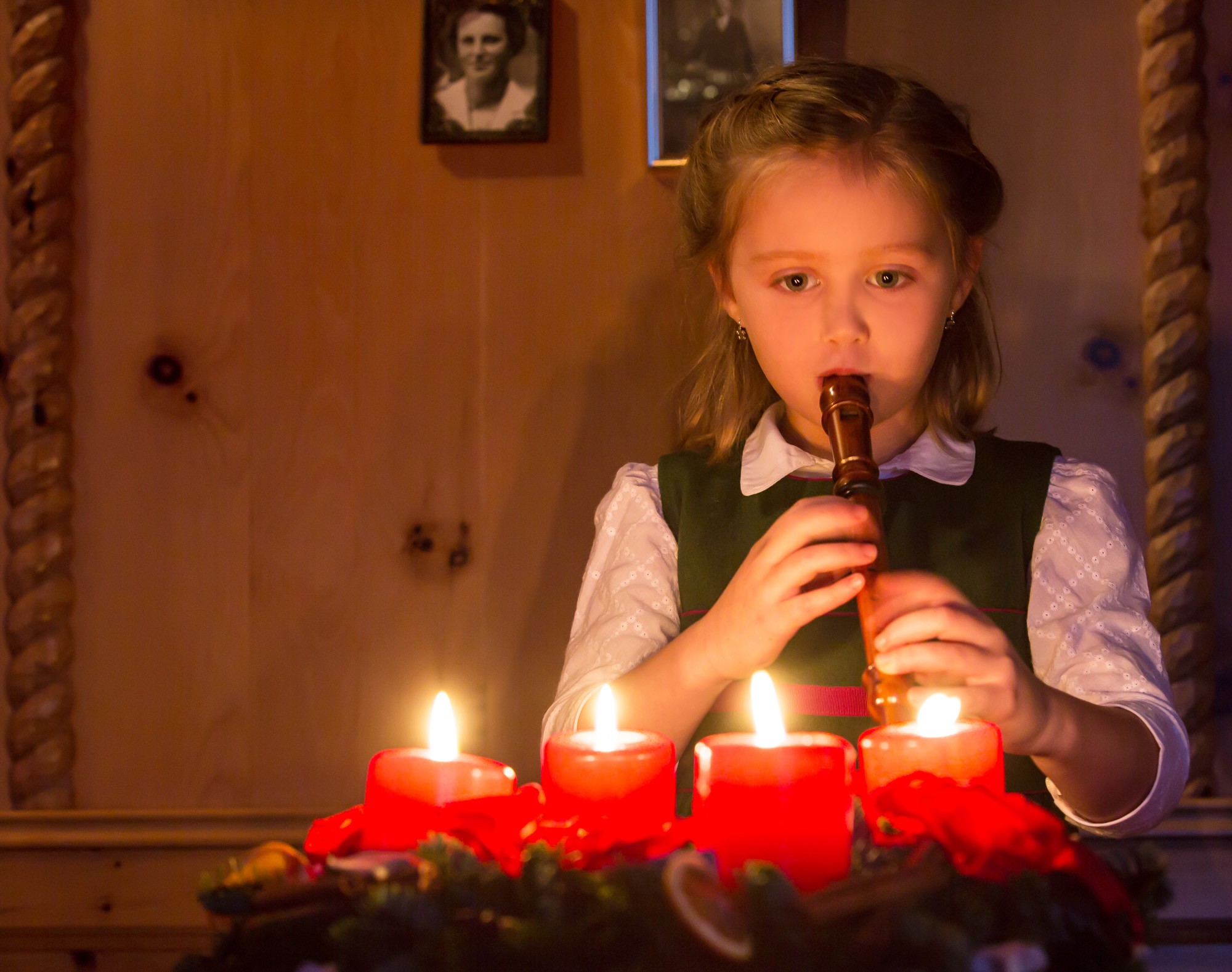 Una bambina suona il flauto davanti a 4 candele rosse accese